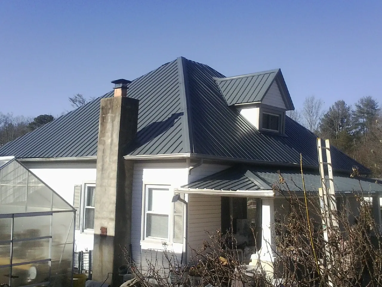 Dark blue standing seam metal roof on a white farmhouse with dormer — Slate & Tile Roof Repair by Roofing Brothers in Sand Coulee