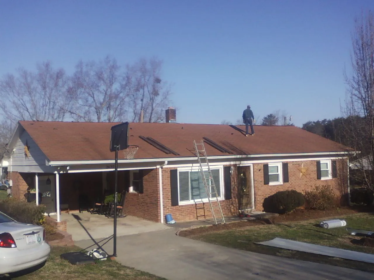 Roofer stripping a shingle roof on a brick ranch before metal panels in Sand Coulee