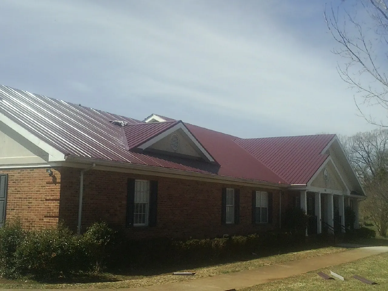 Red metal roof with gabled entries on a long brick building, from a Hail Damage Roof Repair job in Sand Coulee