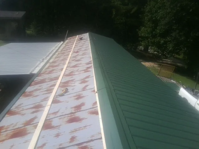 Old rusted panels beside newly installed green metal roofing — Wind Damage Roof Repair by Roofing Brothers in Sand Coulee