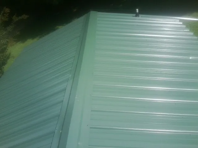 New green metal panels meeting at the ridge of a roof — Flat Roof Repair work by our crew in Sand Coulee