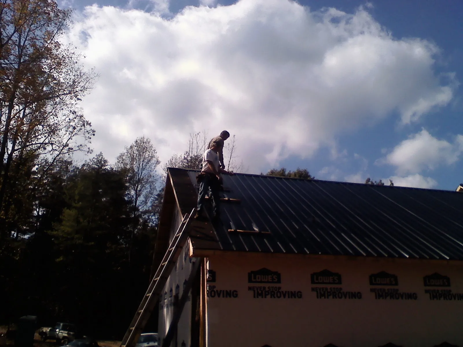 Roofer fastening dark metal panels high against a cloudy sky, from a Roof Inspection job in Sand Coulee